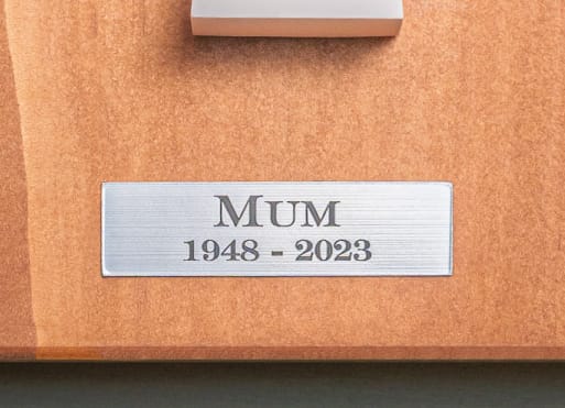 An engraved silver name plaque on a wooden memorial board