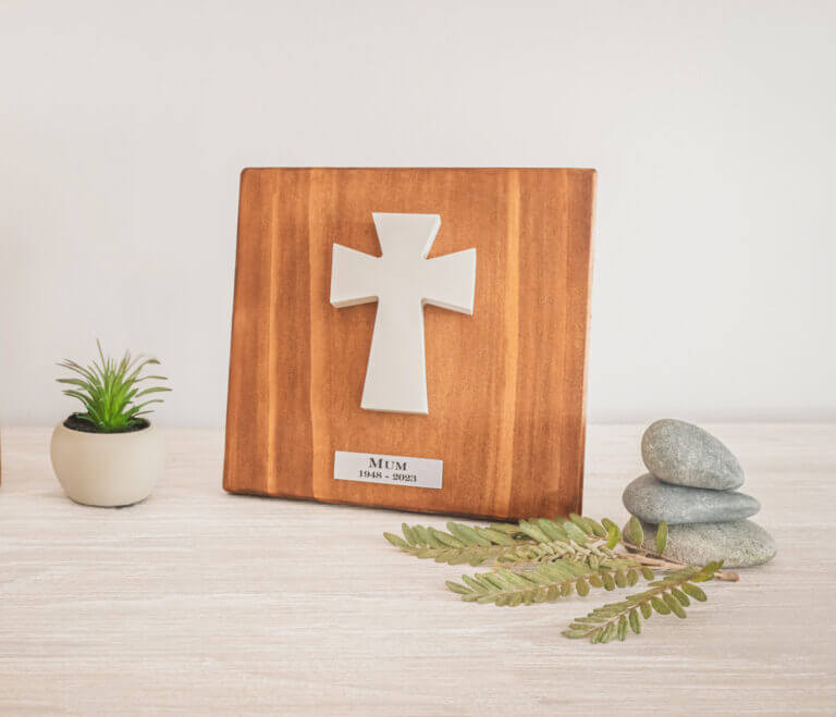 A wooden memorial plaque with a white cross, engraved “Mum, 1948–2023”